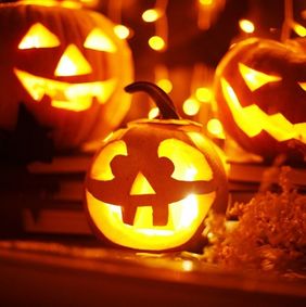 Drei leuchtende Halloween-Kürbisse mit geschnitzten Gesichtern in unterschiedlicher Größe, unscharfer Hintergrund mit Lichterketten